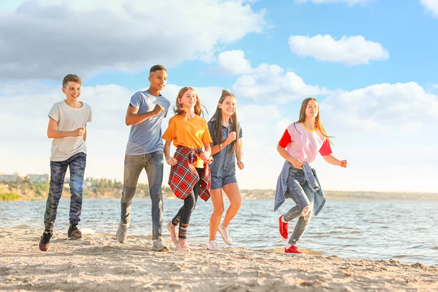 A group of children of various ages and races happily run along the beach. Get concierge primary care for children from The Cove Concierge Medicine in Denver.