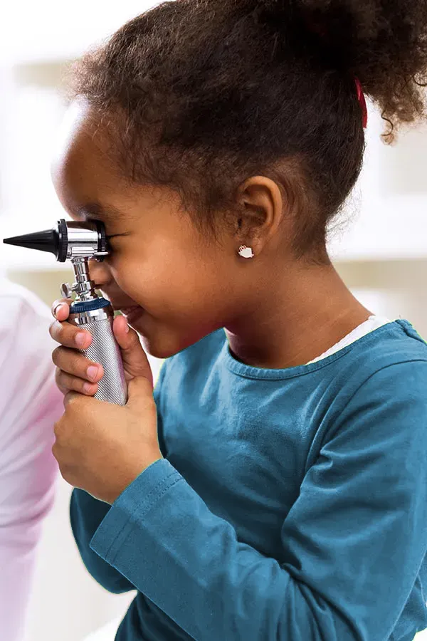 A very young African-American girl plays with an ear examiner at the the doctor's office. Get concierge primary care for children from The Cove Concierge Medicine in Denver.