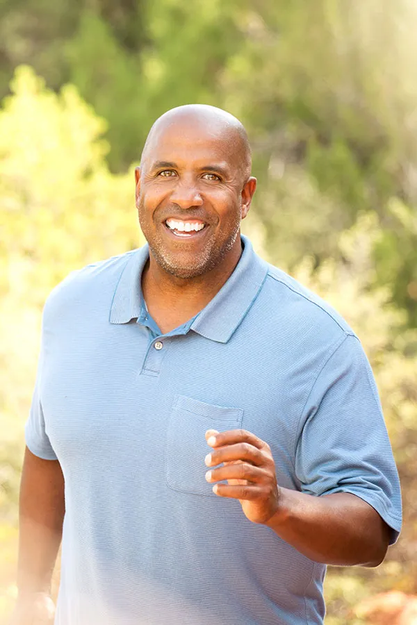 An African-American man in a light blue polo shirt jogs outside. Get concierge primary care for men from The Cove Concierge Medicine in Denver.