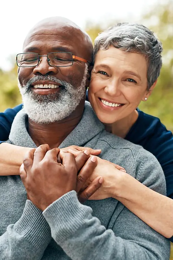 A mature mixed-race couple embrace and bask in the healthy outdoor sky. Get concierge primary care for seniors from The Cove Concierge Medicine in Denver.