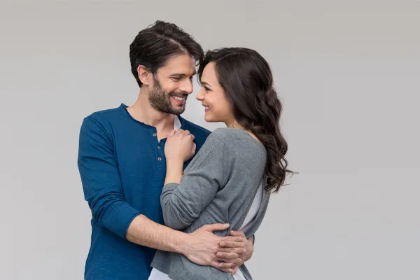 A man in a blue shirt embracing a woman in a gray shirt smiles due to his successful erectile dysfunction care from The Cove Concierge Medicine in Denver.