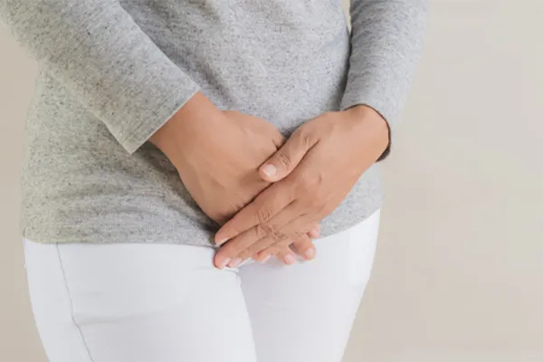 Close up of a woman in a gray shirt and white pants holding her hands below her abdomen in discomfort. Get treatment for fibroids from The Cove Concierge Medicine in Denver.