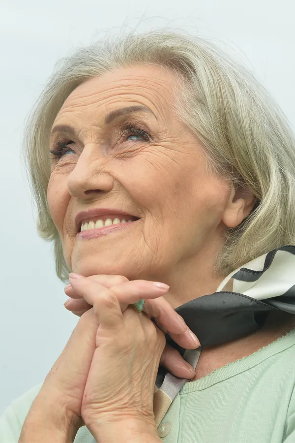 An older woman holds her hands together under her chin and looks up at a cool sky smiling. Get treatment for hot flashes and night sweats from The Cove Concierge Medicine in Denver.
