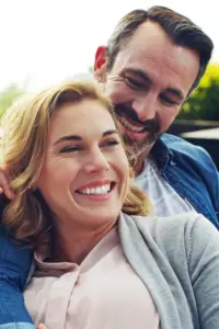 A middle-aged couple laugh and embrace while sitting outside. Get nest genomics testing from The Cove Concierge Medicine in Denver.