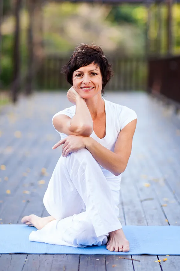 A middle-aged woman happily sits in a yoga pose. Get Osteoporosis treatment from The Cove Concierge Medicine in Denver.