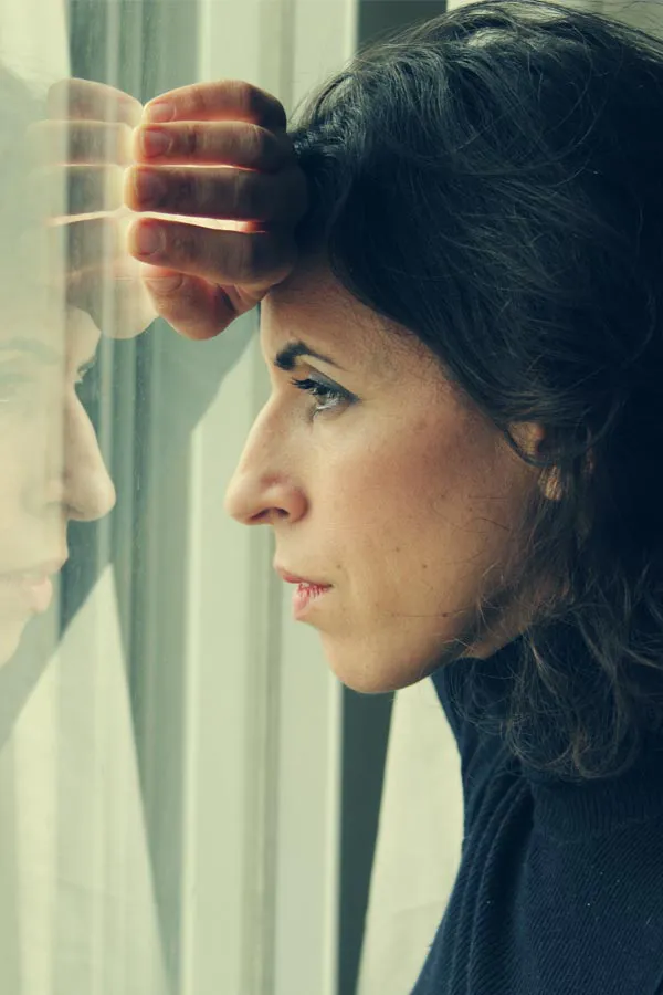 A brunette woman in a thin dark turtleneck looks out the window with a serious expression, suffering from PCOS. Get treatment for Polycistic Ovarian Syndrome/PCOS from The Cove Concierge Medicine in Denver.