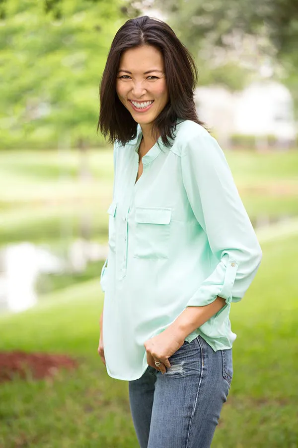 A middle-aged brunette woman in a light green button-up shirt stands outside smiling, happy with her perimenopause treatment from The Cove Concierge Medicine in Denver.