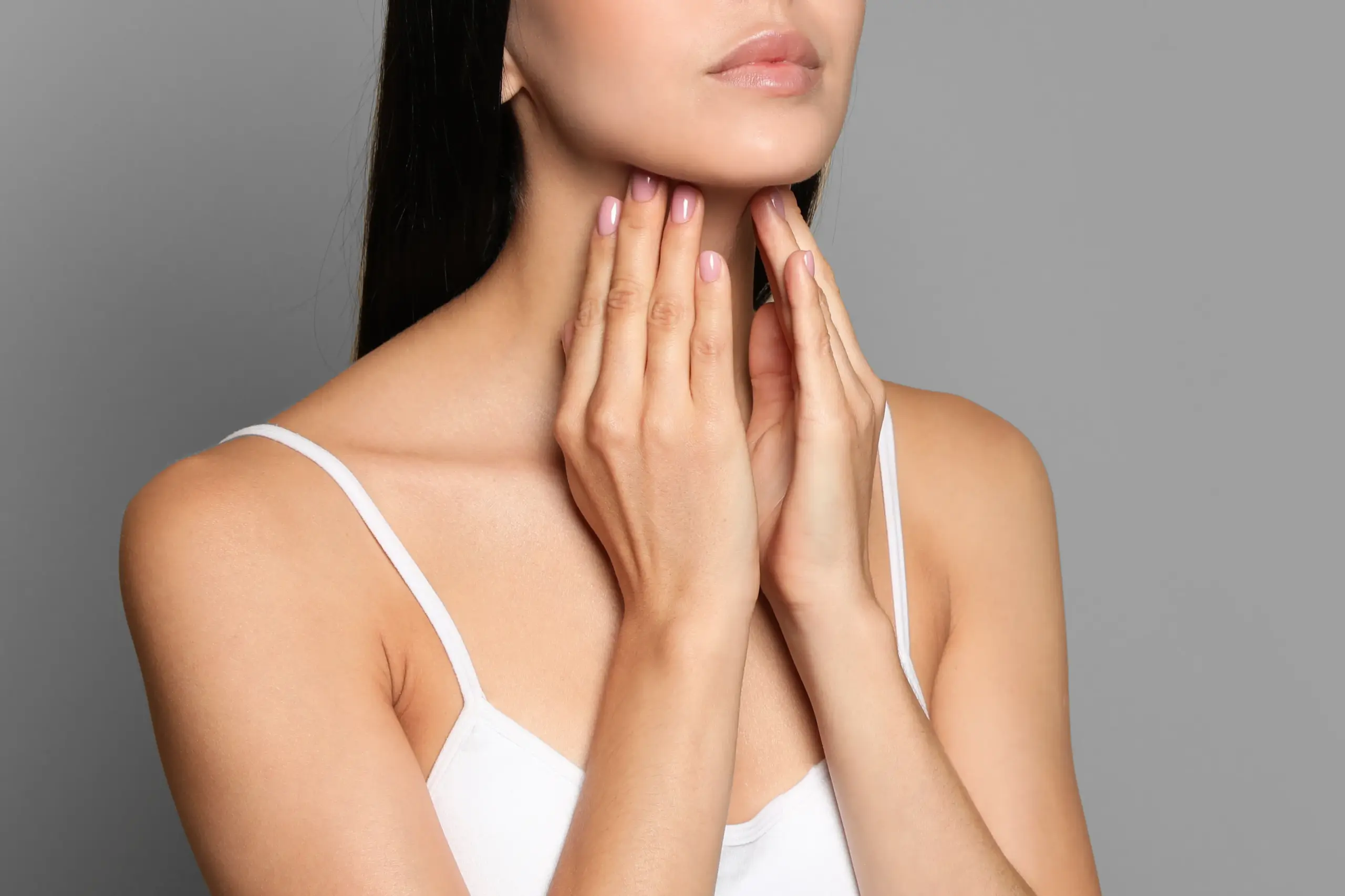A woman in a white tank top touches her neck looking for signs of thyroid disorder. Get help for thyroid disorders from The Cove Concierge Medicine in Denver.